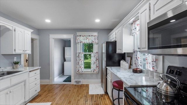 kitchen with white cabinetry, sink, light stone countertops, black range with electric cooktop, and light hardwood / wood-style flooring