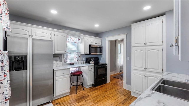 kitchen with white cabinets, sink, light hardwood / wood-style floors, light stone counters, and stainless steel appliances