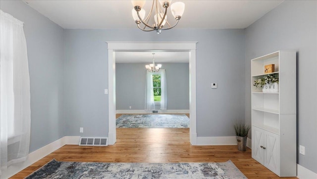 empty room with a notable chandelier and wood-type flooring