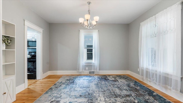 empty room with light wood-type flooring and an inviting chandelier