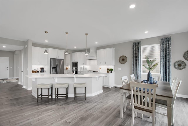 kitchen with stainless steel fridge, premium range hood, a large island with sink, white cabinetry, and hanging light fixtures