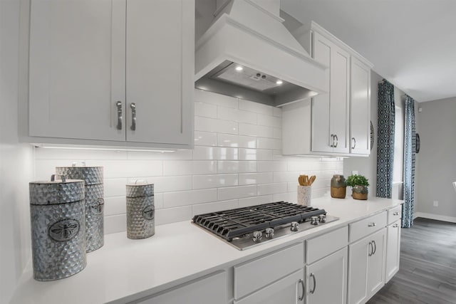 kitchen with dark wood-type flooring, custom range hood, tasteful backsplash, white cabinetry, and stainless steel gas cooktop