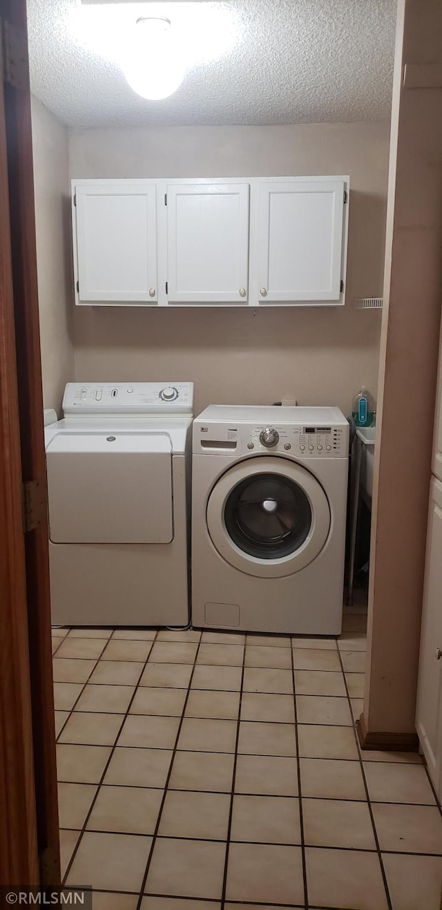 clothes washing area featuring washing machine and dryer, cabinets, a textured ceiling, and light tile patterned flooring