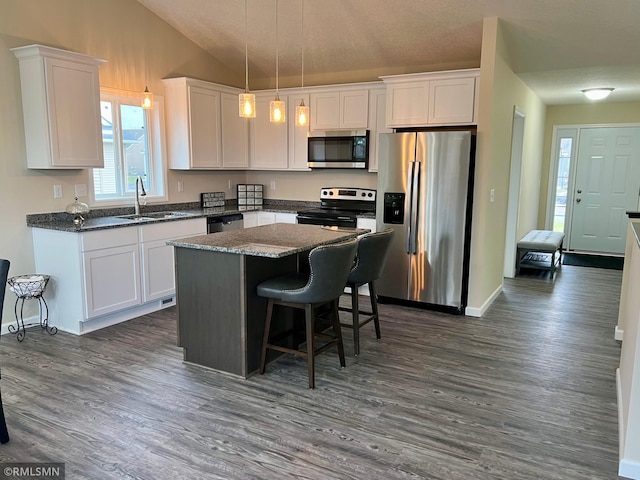 kitchen featuring dark wood-type flooring, vaulted ceiling, appliances with stainless steel finishes, decorative light fixtures, and white cabinetry