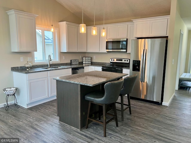 kitchen featuring stainless steel appliances, vaulted ceiling, sink, white cabinets, and hanging light fixtures