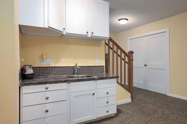 kitchen featuring a textured ceiling, white cabinetry, dark carpet, and sink