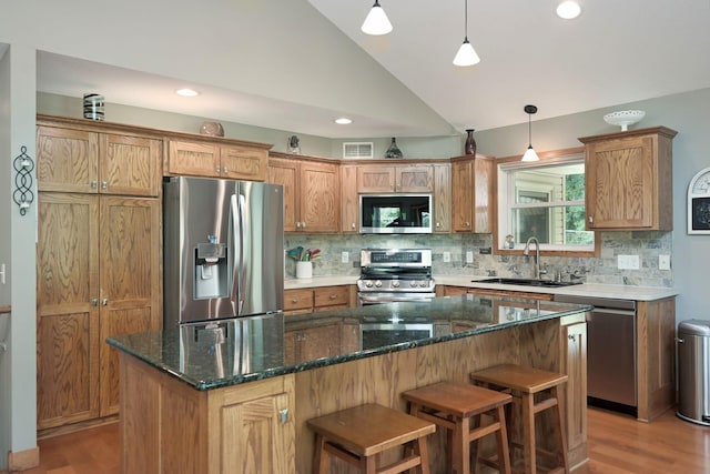 kitchen featuring lofted ceiling, decorative light fixtures, a center island, sink, and appliances with stainless steel finishes