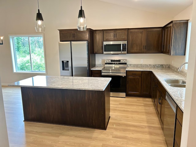 kitchen with stainless steel appliances, pendant lighting, light hardwood / wood-style flooring, light stone counters, and sink