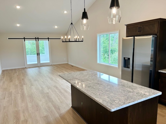 kitchen with stainless steel fridge, decorative light fixtures, light wood-type flooring, light stone counters, and dark brown cabinetry