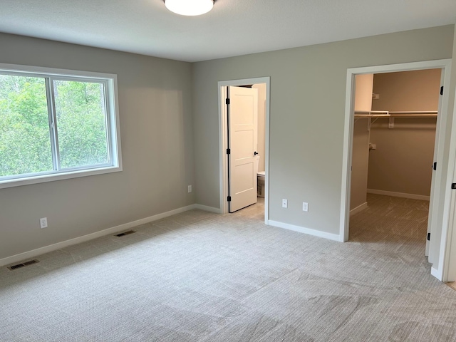 unfurnished bedroom with light carpet, a walk in closet, a closet, and ensuite bathroom