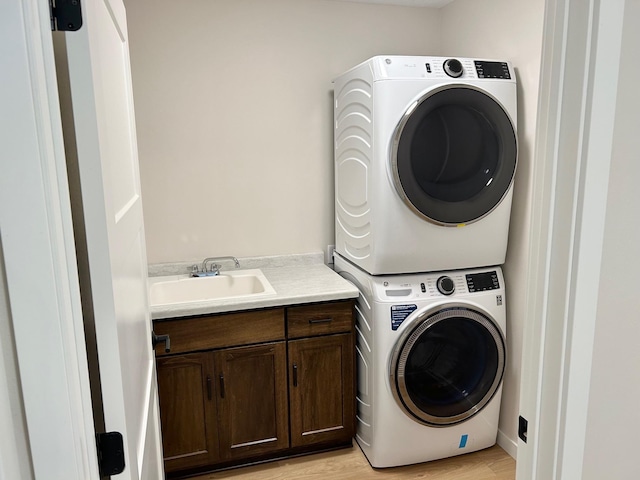 clothes washing area with cabinets, stacked washer / drying machine, light hardwood / wood-style flooring, and sink