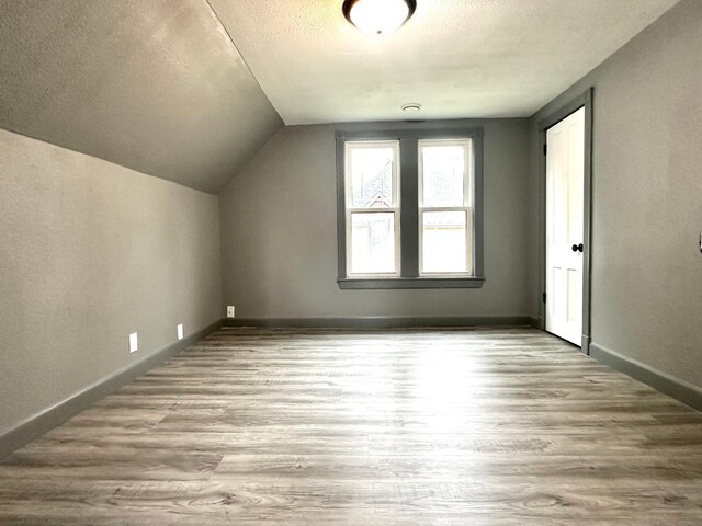 additional living space with a textured ceiling, lofted ceiling, and hardwood / wood-style floors