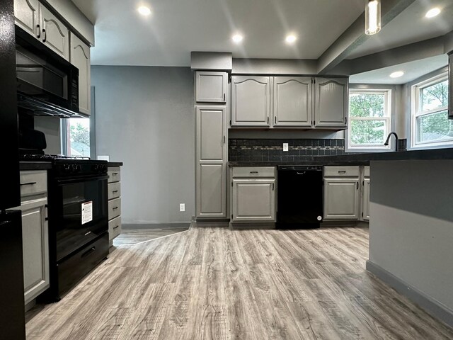 kitchen with gray cabinets, light hardwood / wood-style floors, backsplash, and black appliances