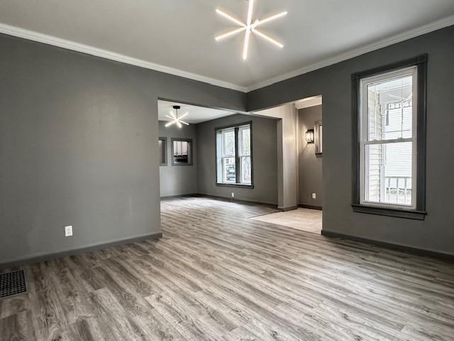 unfurnished living room with light wood-type flooring, ornamental molding, and a healthy amount of sunlight