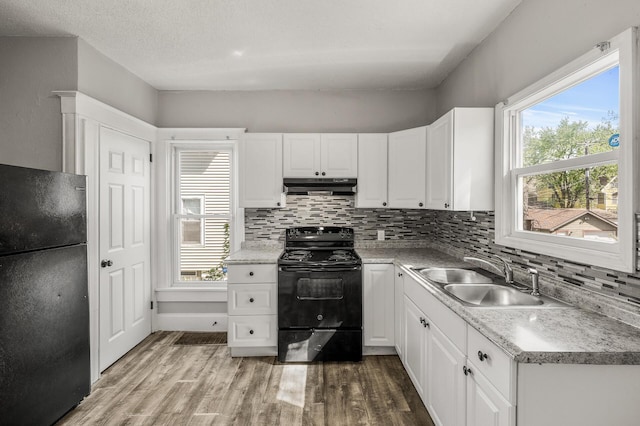 2806 Aldrich Ave N, Minneapolis, MN 55411 - kitchen featuring black appliances, a sink, under cabinet range hood, light wood finished floors, and tasteful backsplash