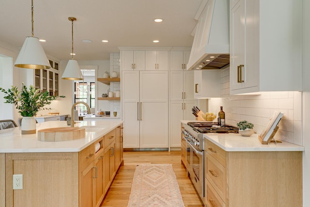 kitchen with light hardwood / wood-style flooring, tasteful backsplash, double oven range, premium range hood, and sink