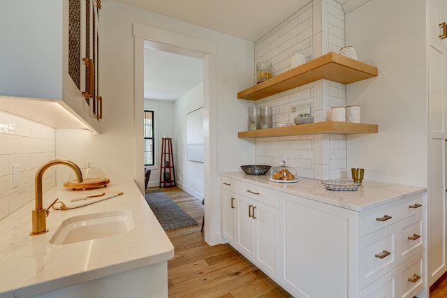 kitchen with light hardwood / wood-style floors, white cabinetry, light stone countertops, sink, and tasteful backsplash