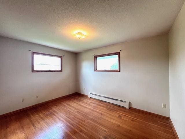 empty room with a textured ceiling, plenty of natural light, hardwood / wood-style floors, and baseboard heating