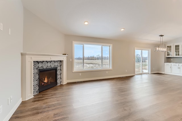 unfurnished living room featuring hardwood / wood-style floors, a healthy amount of sunlight, vaulted ceiling, and a tiled fireplace