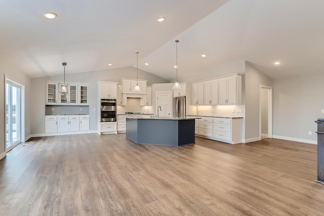 kitchen featuring white cabinetry, stainless steel appliances, pendant lighting, vaulted ceiling, and a center island with sink