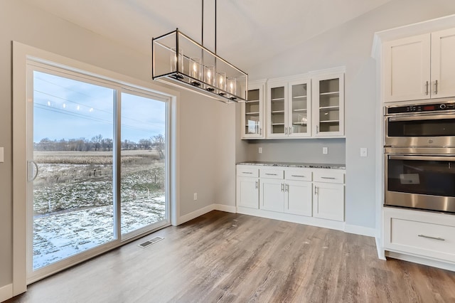 kitchen featuring white cabinets, vaulted ceiling, light stone countertops, double oven, and light hardwood / wood-style floors