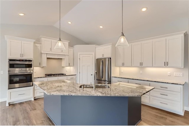 kitchen with appliances with stainless steel finishes, vaulted ceiling, sink, pendant lighting, and an island with sink