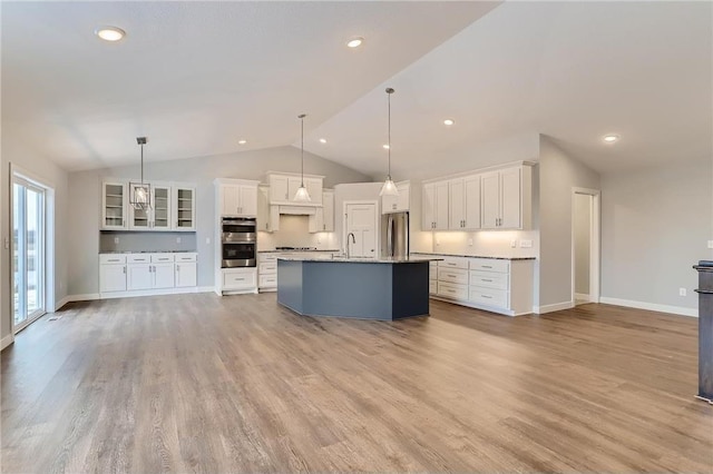 kitchen with lofted ceiling, light hardwood / wood-style flooring, an island with sink, decorative light fixtures, and stainless steel appliances