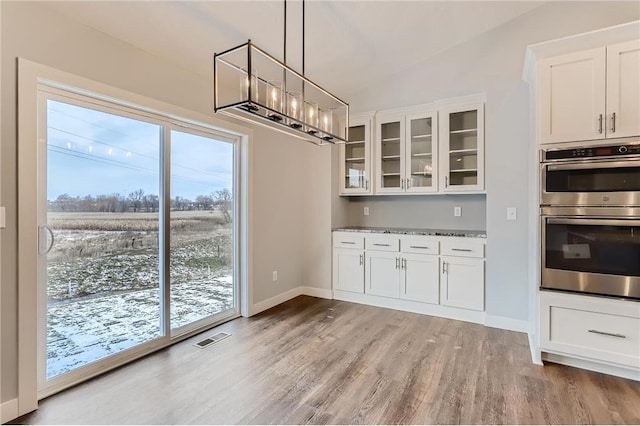 kitchen with vaulted ceiling, light wood-type flooring, double oven, light stone counters, and white cabinetry