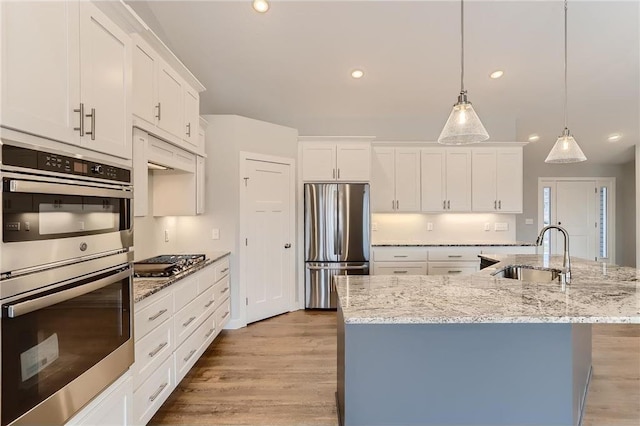 kitchen featuring appliances with stainless steel finishes, decorative light fixtures, a kitchen island with sink, and sink