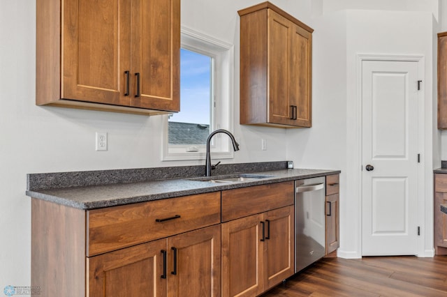 kitchen featuring stainless steel dishwasher, brown cabinetry, dark stone countertops, a sink, and dark wood-style floors