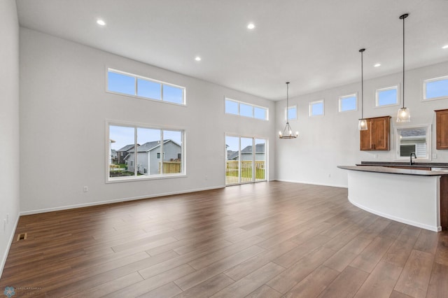 unfurnished living room featuring baseboards, a high ceiling, a chandelier, recessed lighting, and dark wood-type flooring