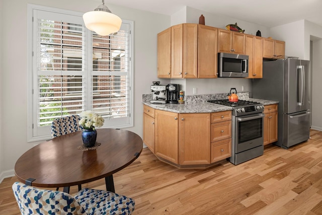 kitchen featuring appliances with stainless steel finishes, light hardwood / wood-style flooring, light stone countertops, and pendant lighting