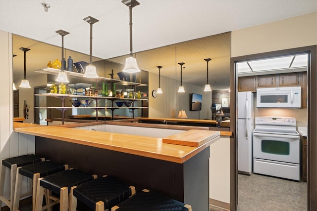 kitchen featuring a breakfast bar area, hanging light fixtures, white appliances, and wood counters