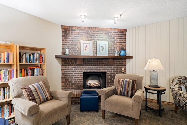 sitting room featuring a textured ceiling, wooden walls, and a brick fireplace