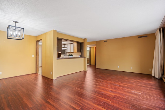 unfurnished living room with a notable chandelier, dark hardwood / wood-style flooring, and a textured ceiling