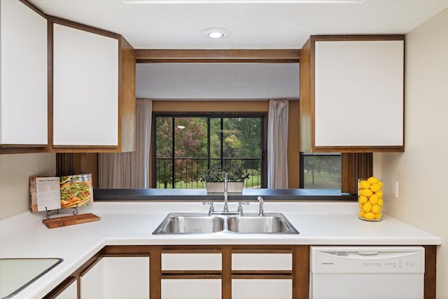 kitchen with white dishwasher, white cabinets, and sink