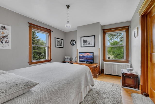 bedroom with radiator heating unit, multiple windows, and light hardwood / wood-style flooring