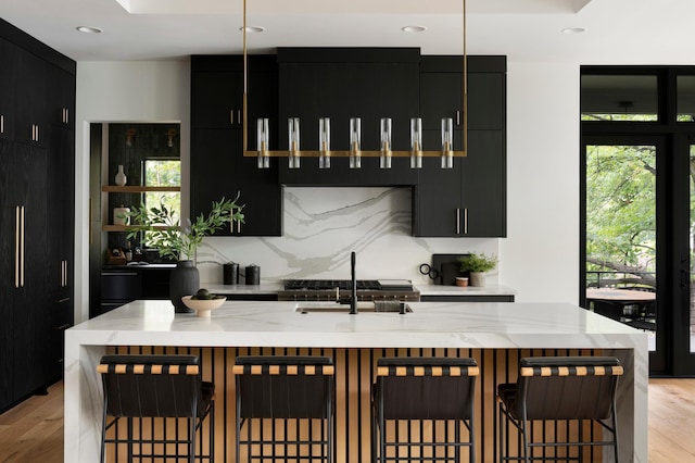 kitchen with backsplash, a breakfast bar area, light hardwood / wood-style floors, and an island with sink