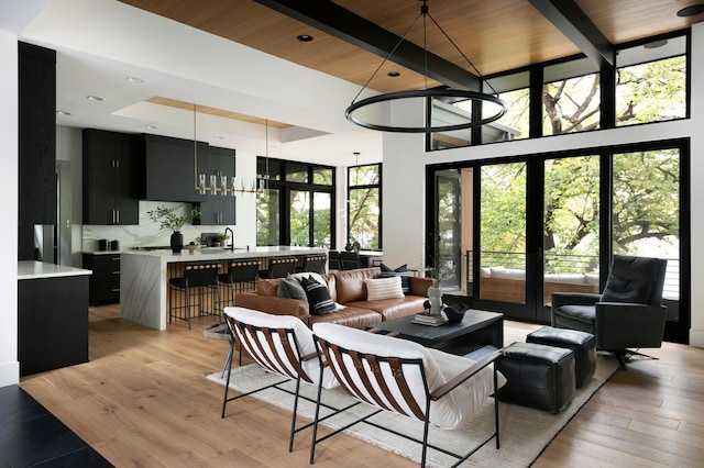 living room with french doors, beam ceiling, sink, and light wood-type flooring