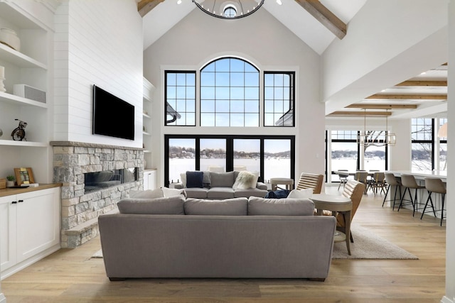 living room with beamed ceiling, a fireplace, light hardwood / wood-style floors, and a notable chandelier