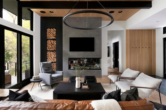 living area with a towering ceiling, wood ceiling, recessed lighting, beamed ceiling, and a glass covered fireplace