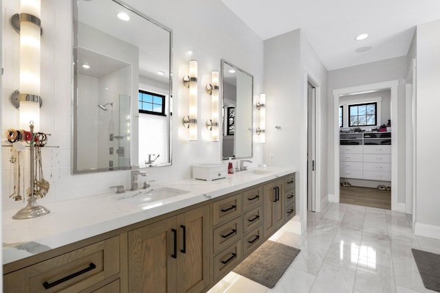 bathroom with a tile shower, double vanity, baseboards, a spacious closet, and marble finish flooring