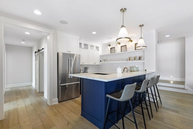 kitchen featuring high end fridge, a barn door, open shelves, a kitchen breakfast bar, and white cabinetry