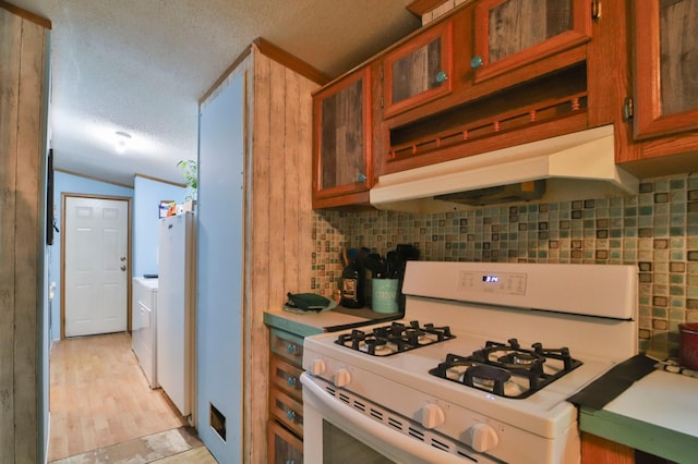 kitchen featuring white appliances, a textured ceiling, washer / dryer, backsplash, and vaulted ceiling