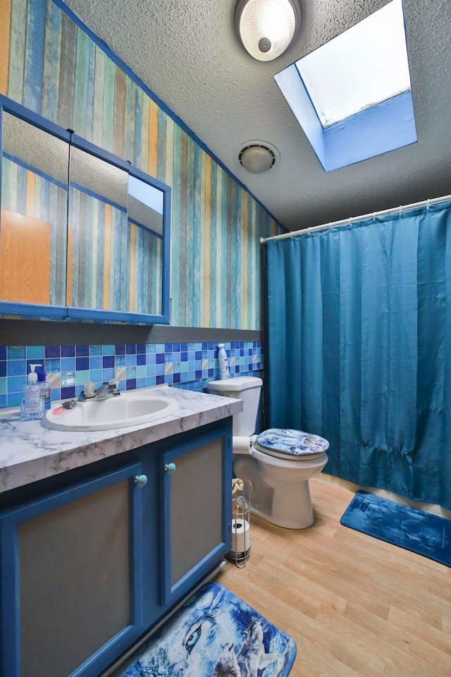 bathroom with wood-type flooring, vanity, a skylight, decorative backsplash, and toilet