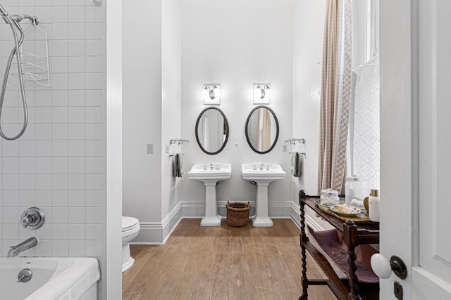 bathroom featuring baseboards, toilet, wood finished floors, tub / shower combination, and a sink