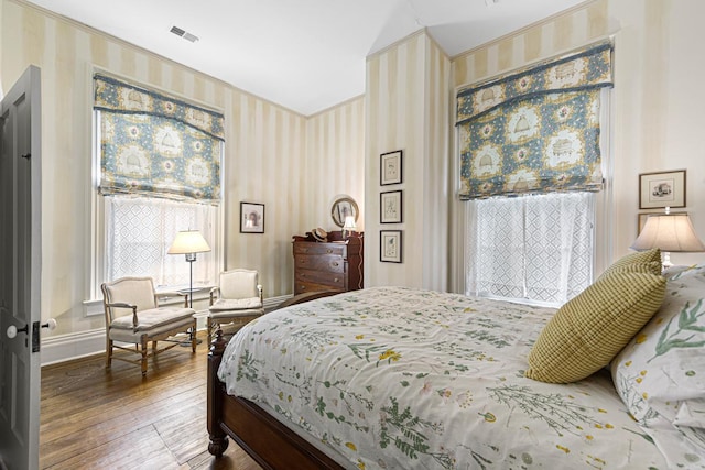 bedroom with baseboards, visible vents, wallpapered walls, and wood finished floors