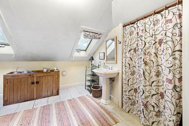 full bathroom with vaulted ceiling with skylight, a sink, and baseboards