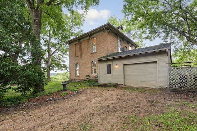 back of house with dirt driveway, a chimney, an attached garage, fence, and brick siding