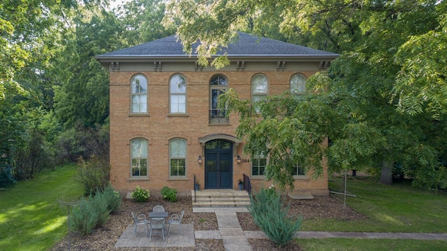 italianate house featuring brick siding, roof with shingles, a patio area, and a front yard